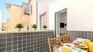 A balcony with a table set for breakfast, potted plants, and a view of a building. - Olarias Terrace Lisbon III (Lisbon)