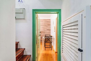 Ein schmaler Flur mit einem grünen Türrahmen, einer Treppe, einem Esstisch mit Stühlen und einem Fenster mit Jalousien.