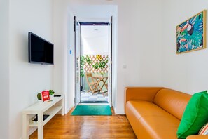 A living room with a sofa, a TV, a small table with a cactus, and a door leading to a balcony with plants. - Olarias Terrace Lisbon IV (Lisbon)