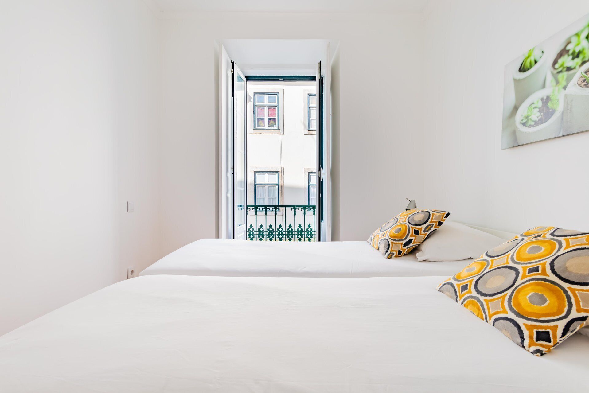Une chambre à coucher avec un lit, des oreillers, une porte donnant sur un balcon extérieur et un tableau accroché au mur.