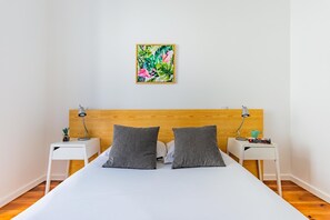 A bedroom with a wooden headboard, two bedside tables with lamps, a bed with grey pillows, and a wall-mounted picture. - Olarias Terrace Lisbon IV (Lisbon)