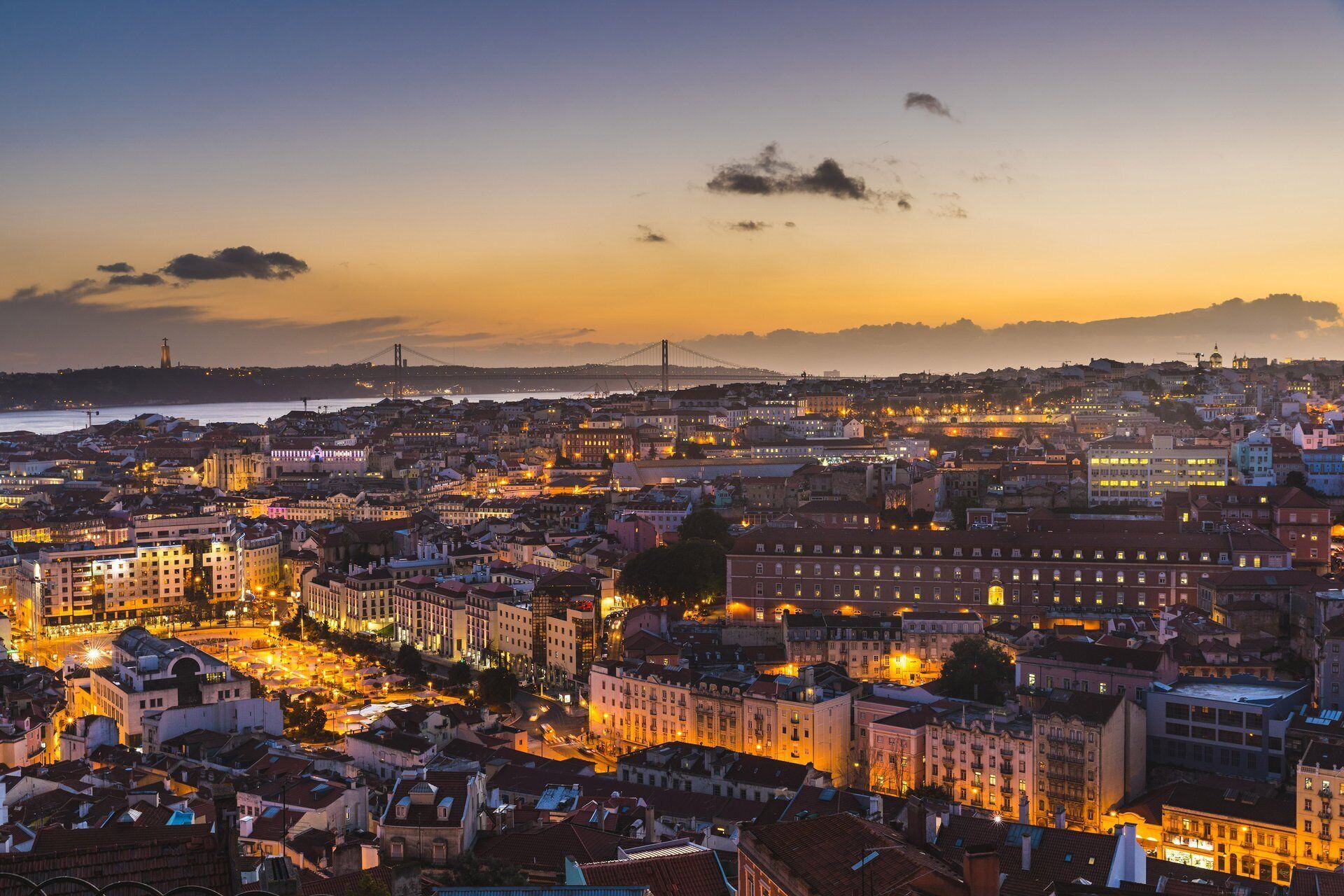 Une vue d’une ville au crépuscule, avec des bâtiments illuminés et un pont au loin.