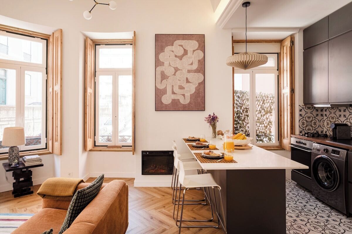 A modern kitchen with a central island, large windows, and a dining area with a sofa.