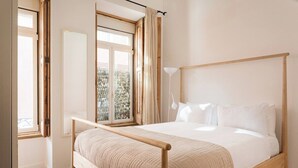 Une chambre à coucher avec un lit en bois, une fenêtre avec des rideaux, une lampe de chevet et une vue sur la verdure à l’extérieur.