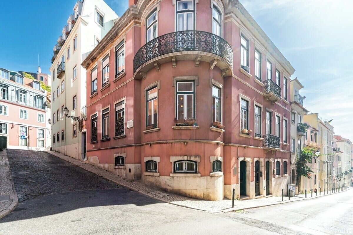 Un immeuble d’angle doté d’un balcon incurvé, de nombreuses fenêtres et situé sur une rue pavée.