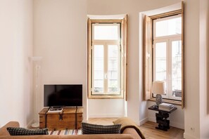 A living room with a TV, wooden furniture, and large windows. - Principe Real Urban Heaven (Lisbon)