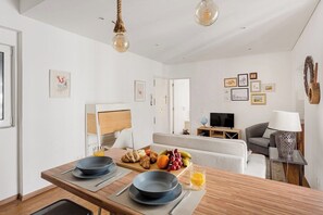 Ein modernes Hotelzimmer mit Essbereich, einer Couch, einem Fernseher und Kunstwerken an den Wänden.