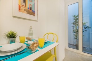 A dining table with plates, cutlery, a glass of orange juice, a bottle, and a bowl of cereal. There is a potted plant and a yellow chair. - Tram Hideaway | Bica Stay (Lisbon)