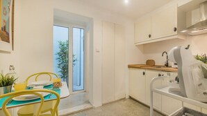 Cuina moderna amb armaris blancs, un rentapeus i zona de menjador amb cadires grogues i una taula.