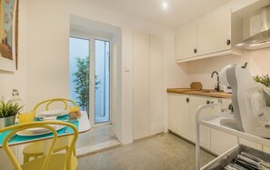 A modern kitchen with white cabinets, a sink, and a dining area with yellow chairs and a table. - Tram Hideaway | Bica Stay (Lisbon)
