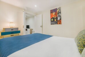 A bedroom with a bed, a nightstand, a lamp, a poster on the wall, and a door leading to another room. - Tram Hideaway | Bica Stay (Lisbon)