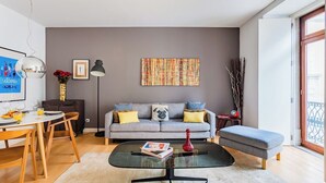 Ein modernes Wohnzimmer mit einem grauen Sofa, einem Glastisch und einem Essbereich mit einem Holztisch und Stühlen.