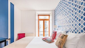 Ein Hotelzimmer mit einem Bett, einem roten Sessel, einem Fenster mit Ausblick und Wandtapete mit Muster.