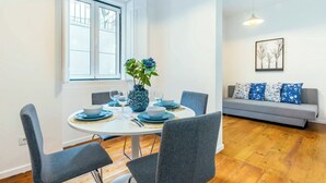 En spiseplads med et rundt bord, grå stole, en vase med blomster og en grå sofa med mønstrede puder.