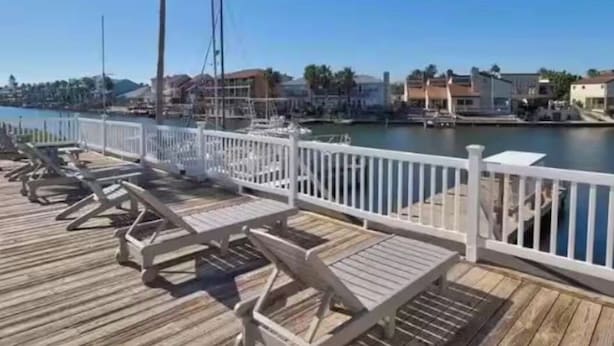 A wooden pier with lounge chairs and a white railing, overlooking a marina with boats and buildings in the background. - Quaint 1-bedroom island condo in Corpus Christi with all the comforts of home. (Corpus Christi)