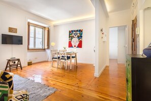 A room with wooden flooring, a dining table with chairs, a television mounted on the wall, and a painting above the table. - Chiado Central Apartment, the Heart of Lisbon (Lisbon)