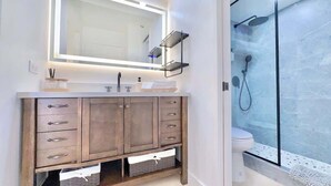 Un baño moderno con tocador, espejo grande, cabina de ducha e inodoro.