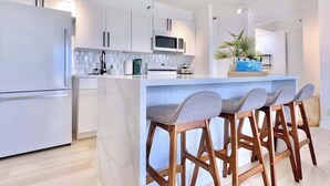 Una cocina moderna con muebles blancos, una isla central con taburetes y un microondas.