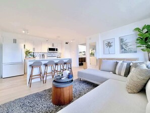 Ein modernes Wohnzimmer mit einer Couch, einem Couchtisch und einer Küchenzeile im Hintergrund.