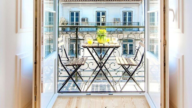 En åben balkon med udsigt til en bygning med røde skodder og et tagtækket tag.
