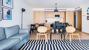 Ein modernes Wohnzimmer mit einer Couch, einem Essbereich mit Stühlen, einer Küche mit Schränken und Geräten, und einem schwarz-weißen Streifen Teppich.