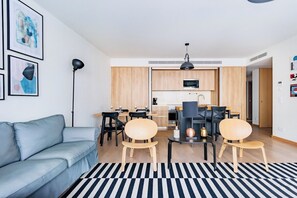 Ein modernes Wohnzimmer mit einer Couch, einem Essbereich mit Stühlen, einer Küche mit Schränken und Geräten, und einem schwarz-weißen Streifen Teppich.