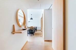 Ein modernes Interieur mit Holzboden, einem runden Spiegel, einer Essecke mit Stühlen und Tisch sowie einer hängenden Pendelleuchte.