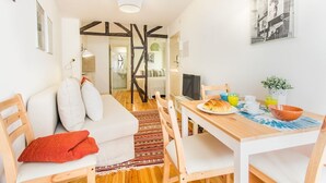Ett modernt vardagsrum med en soffa, ett matbord och stolar. Det står ett tv-apparatt på bordet och en växt hänger på väggen.
