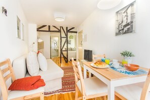 Ein modernes Wohnzimmer mit einer Couch, einem Esstisch und Stühlen. Ein Fernseher steht auf dem Tisch und eine Pflanze ist an der Wand zu sehen.