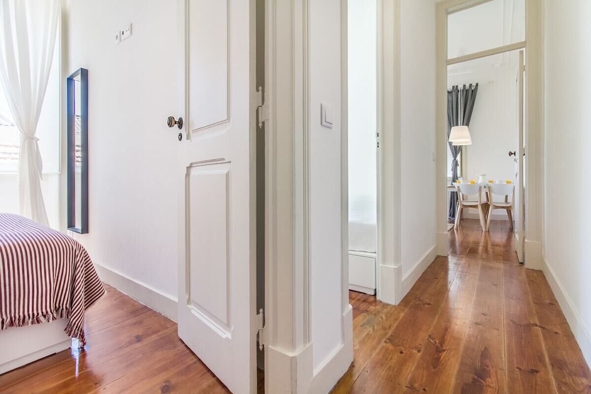 A room with a bed, a door, and a hallway leading to a dining area.