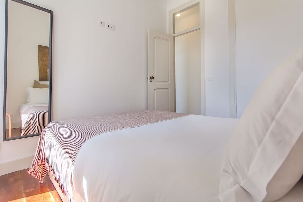 A bedroom with a bed, a mirror, a door, and a light switch on the wall.