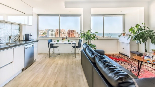 A modern apartment with a kitchen, dining area, and a living room with a view of the city and sea. - Graça Amazing River Views (Lisbon)