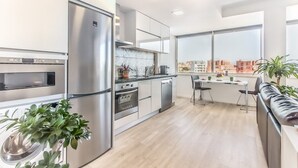 A modern kitchen with stainless steel appliances, a dining area with a view, and a small seating space. - Graça Amazing River Views (Lisbon)