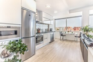 A modern kitchen with stainless steel appliances, a dining area with a view, and a small seating space. - Graça Amazing River Views (Lisbon)