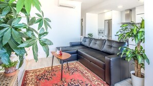 A modern living room with a black leather sofa, a patterned rug, and large green plants. - Graça Amazing River Views (Lisbon)