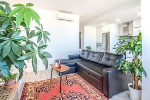 A modern living room with a black leather sofa, a patterned rug, and large green plants. - Graça Amazing River Views (Lisbon)