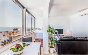 A modern apartment with a balcony, a dining area with a table and chairs, a black leather sofa, a potted plant, and a television. - Graça Amazing River Views (Lisbon)