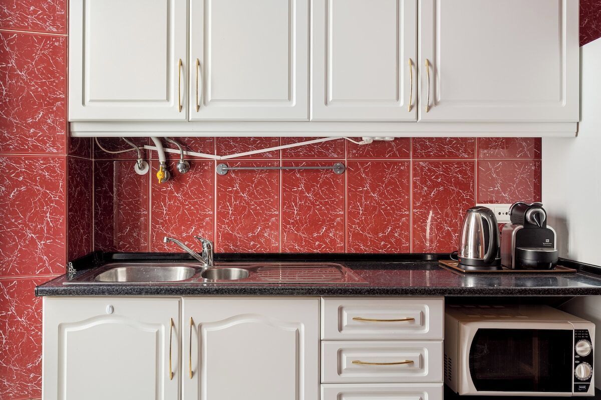 Een keuken met witte kastjes, een zwart aanrecht, een spoelbak, een waterkoker, een broodrooster en een magnetron.