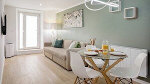 Ein modernes Wohnzimmer mit einer Couch, einem Esstisch mit Stühlen, einer Heizung und einem Wandbild.
