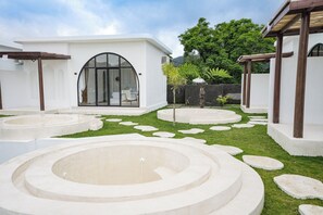 A modern outdoor pool area with circular water features and a white building with a large arched window. - Lazura Serenite (Kintamani)