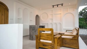 A modern interior with a wooden bench and table, white walls, and a circular skylight. - Lazura Serenite (Kintamani)