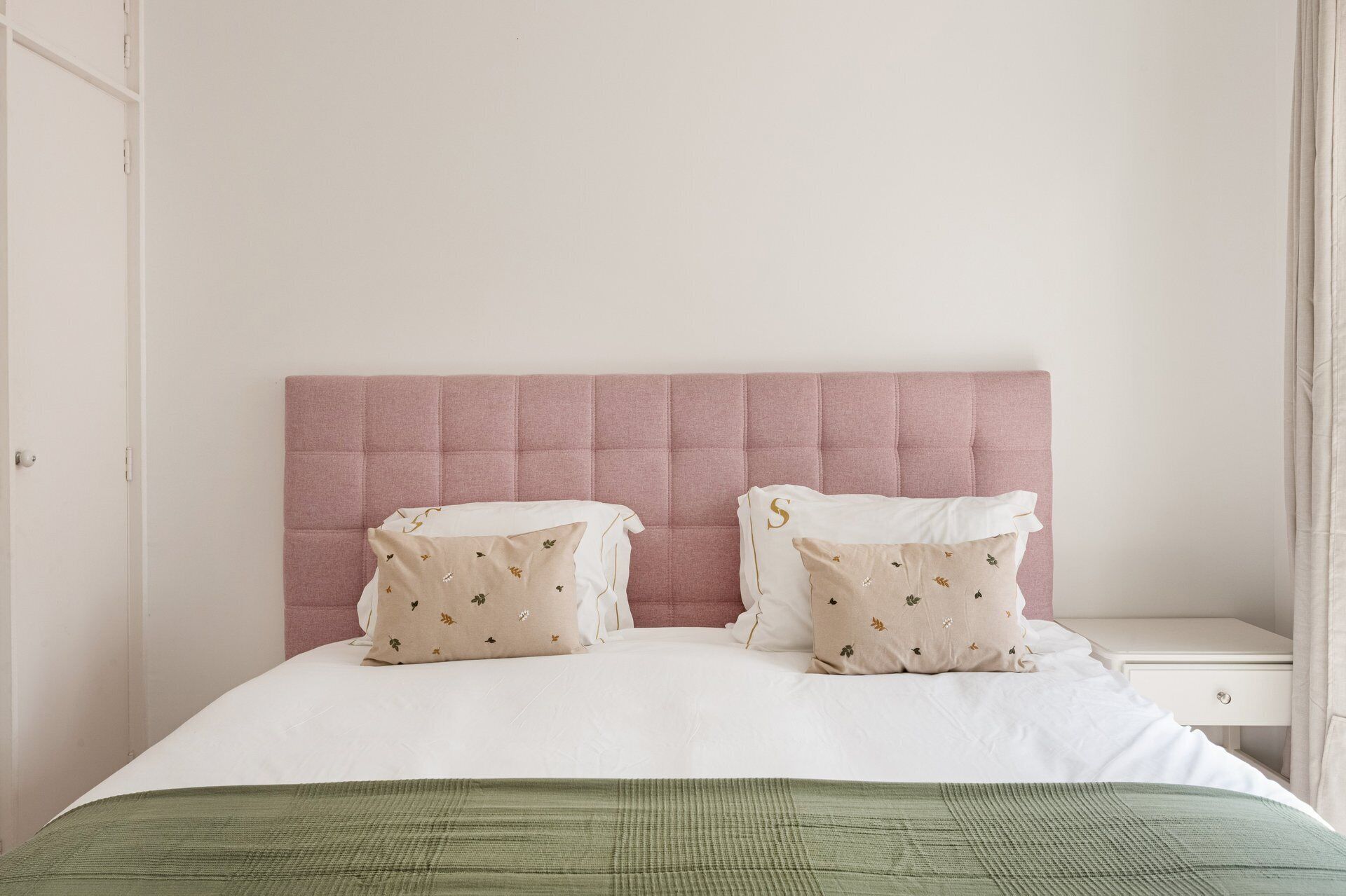 Ein Bett mit rosa Kopfteil, zwei Kissen mit Blumenmuster und einer grünen Decke.