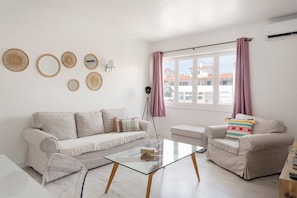 Ein Wohnzimmer mit einer Couch, einem kleinen Sofa, einem Glastisch und einer Stehlampe.