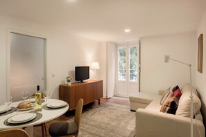 Ein Essbereich mit einem Tisch für zwei Personen, einem Fernseher auf einer Holzkommode und einer Couch im Hintergrund.