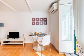 Ein modernes Wohnzimmer mit Flachbildfernseher, einem Esstisch mit Stühlen, einem weißen Sofa und einer weißen Kommode.