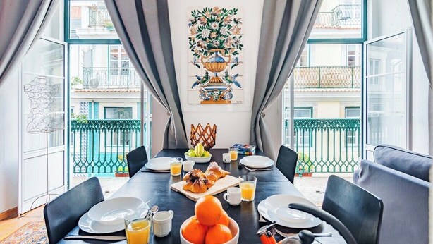 A dining area with a table set for breakfast, a vase with flowers on the wall, and a view of the outside balcony. - Douradores Downtown Flat (Lisbon)