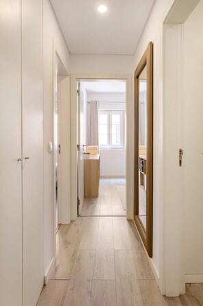 Ein Korridor mit weißen Wänden und Holzboden, der zu einem Zimmer mit Fenster und Holzschrank führt.