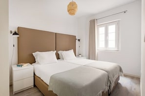Ein Hotelzimmer mit Doppelbett, Nachttischen, einer Lampe, einem Fenster mit Vorhängen und einer Pendelleuchte.