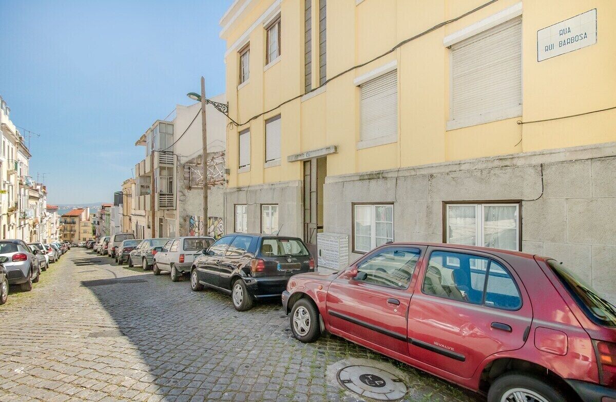 A cobblestone street lined with parked cars and buildings.
