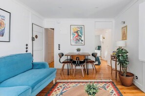 Ein Wohnzimmer mit einem blauen Sofa, einem Holzespeisetisch mit Stühlen, einem gemusterten Teppich und einer Zimmerpflanze.